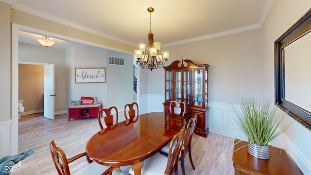 dining space with light wood finished floors, visible vents, wainscoting, ornamental molding, and a notable chandelier