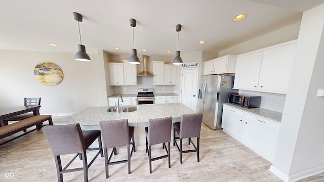 kitchen featuring stainless steel appliances, decorative backsplash, a sink, wall chimney range hood, and a kitchen bar