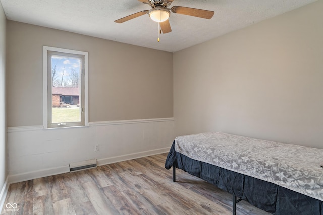 bedroom with a textured ceiling, a wainscoted wall, wood finished floors, visible vents, and a ceiling fan