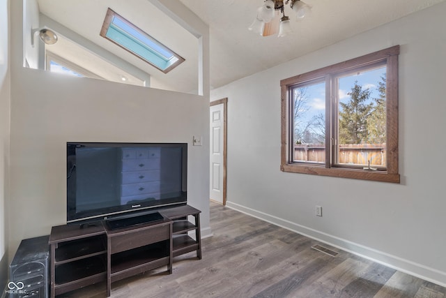 interior space with visible vents, ceiling fan, wood finished floors, vaulted ceiling with skylight, and baseboards