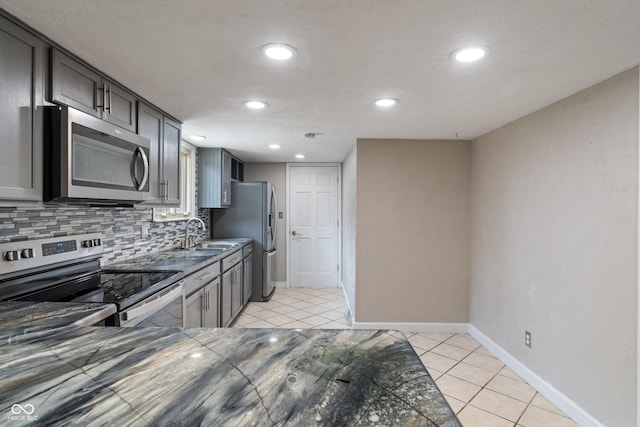 kitchen featuring light tile patterned floors, tasteful backsplash, baseboards, stainless steel appliances, and a sink