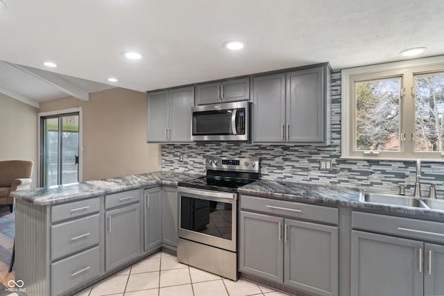 kitchen featuring appliances with stainless steel finishes, decorative backsplash, a peninsula, and gray cabinetry