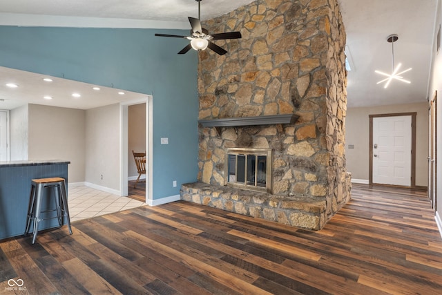 unfurnished living room featuring high vaulted ceiling, a fireplace, wood finished floors, and baseboards