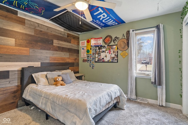 carpeted bedroom with wood walls, ceiling fan, visible vents, and baseboards