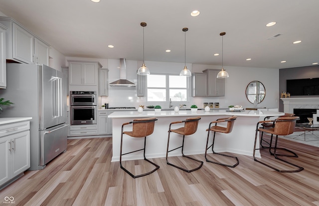 kitchen featuring a breakfast bar area, gray cabinetry, stainless steel appliances, light countertops, and wall chimney exhaust hood