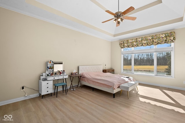 bedroom with a raised ceiling, light wood-style flooring, and baseboards