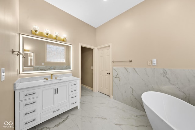 full bath with wainscoting, marble finish floor, vanity, a freestanding tub, and tile walls