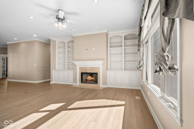 unfurnished living room with light wood-style flooring, a premium fireplace, baseboards, and ornamental molding