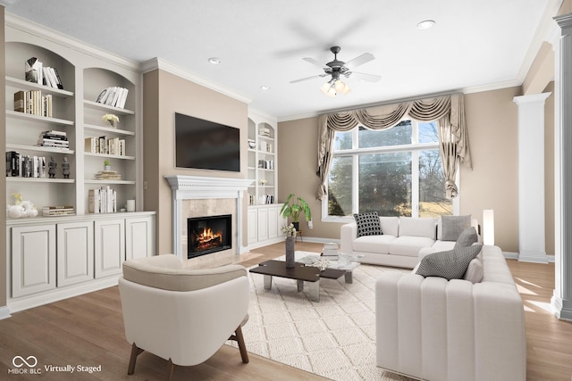 living area featuring wood finished floors, a high end fireplace, baseboards, decorative columns, and crown molding