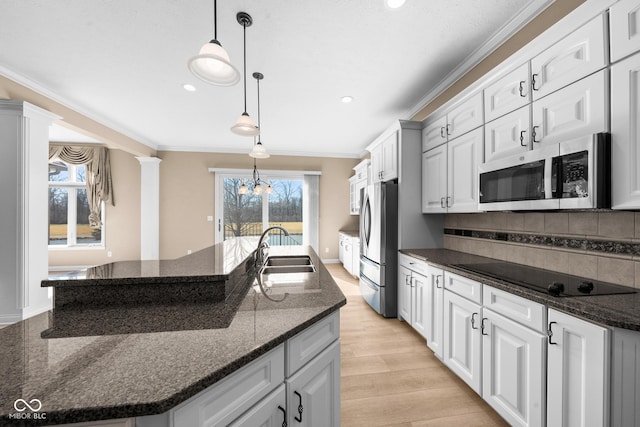 kitchen featuring stainless steel appliances, a sink, decorative columns, a center island with sink, and crown molding