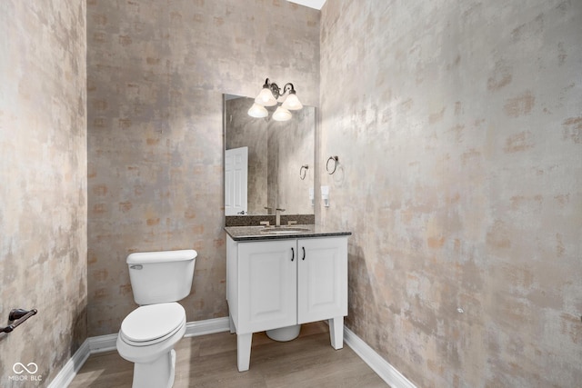 half bathroom featuring baseboards, vanity, toilet, and wood finished floors