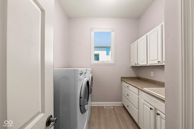 washroom featuring washing machine and dryer, a sink, baseboards, light wood-type flooring, and cabinet space