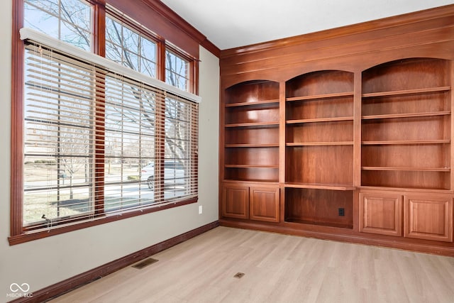 unfurnished room featuring built in shelves, visible vents, ornamental molding, light wood-type flooring, and baseboards