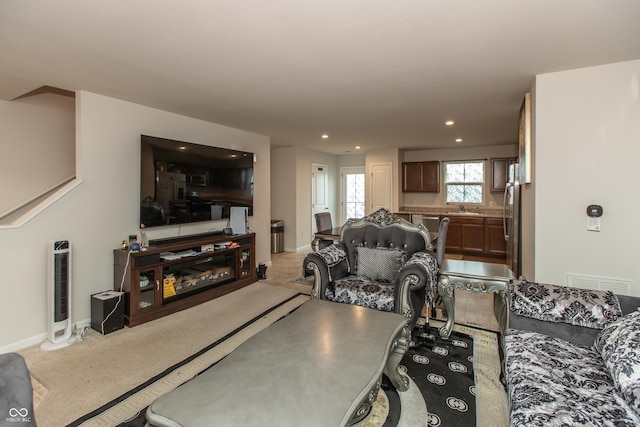 carpeted living room with baseboards, visible vents, a sink, and recessed lighting