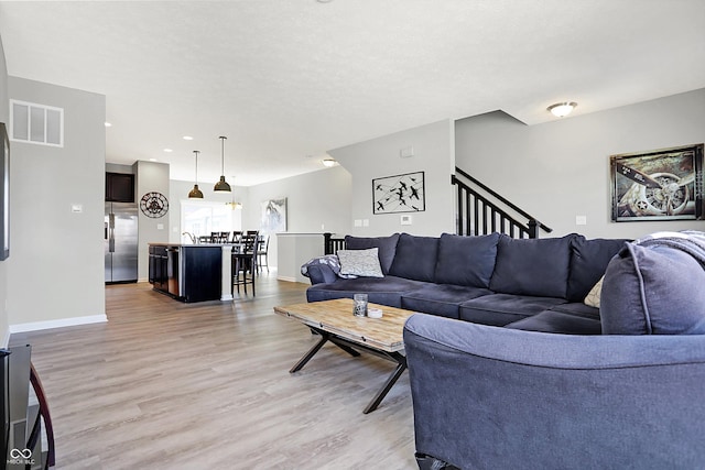 living area with visible vents, light wood-style flooring, stairway, and baseboards