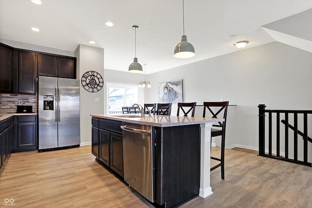 kitchen featuring a kitchen bar, a center island with sink, stainless steel appliances, light wood finished floors, and decorative backsplash