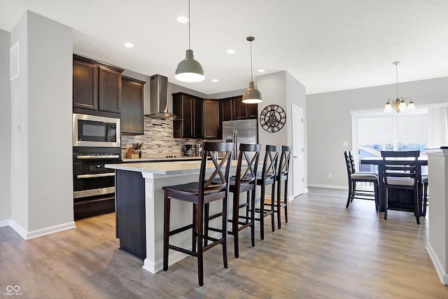 kitchen with light countertops, dark brown cabinets, appliances with stainless steel finishes, wall chimney range hood, and backsplash