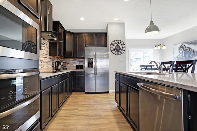 kitchen featuring backsplash, wall chimney range hood, pendant lighting, appliances with stainless steel finishes, and a sink