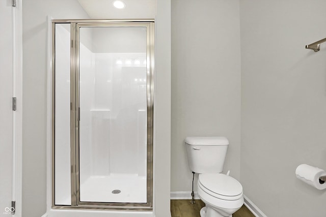 bathroom featuring a shower stall, toilet, wood finished floors, and baseboards