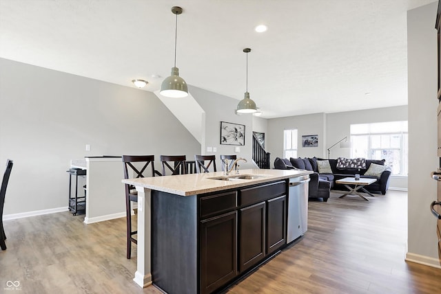 kitchen with stainless steel dishwasher, a breakfast bar area, light wood-style flooring, and a sink