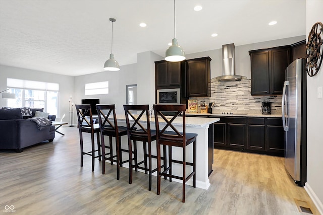 kitchen with a kitchen bar, open floor plan, freestanding refrigerator, wall chimney range hood, and decorative backsplash