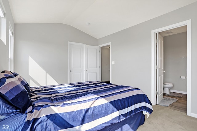 carpeted bedroom featuring visible vents, baseboards, ensuite bathroom, and vaulted ceiling