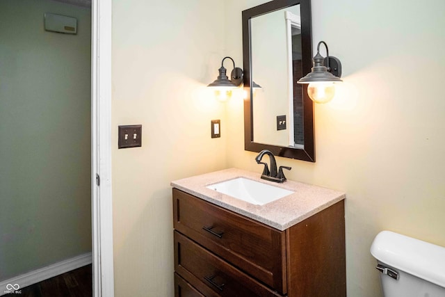 half bathroom with toilet, wood finished floors, vanity, and baseboards