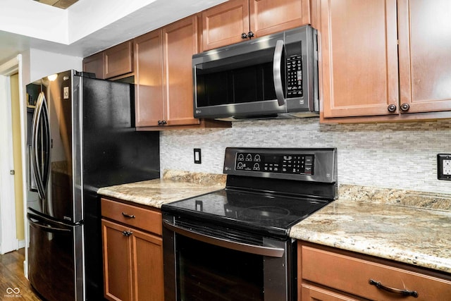 kitchen with brown cabinetry, appliances with stainless steel finishes, dark wood-type flooring, light stone countertops, and backsplash