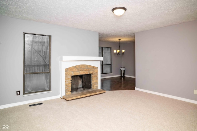 unfurnished living room featuring carpet, a notable chandelier, visible vents, a stone fireplace, and baseboards