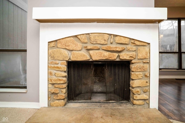 room details featuring a stone fireplace, wood finished floors, and baseboards