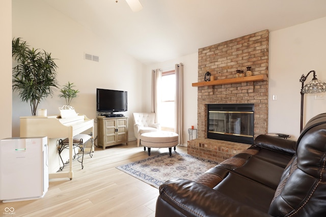 living room featuring lofted ceiling, light wood-style floors, a fireplace, and visible vents