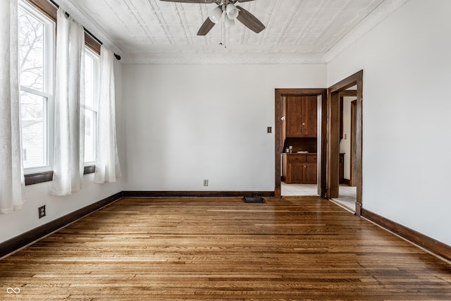 spare room featuring plenty of natural light, wood finished floors, an ornate ceiling, and baseboards