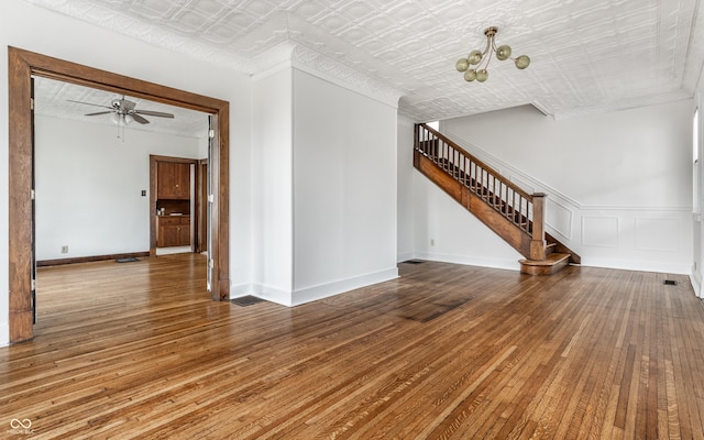 unfurnished living room with ceiling fan with notable chandelier, baseboards, stairs, wood-type flooring, and an ornate ceiling