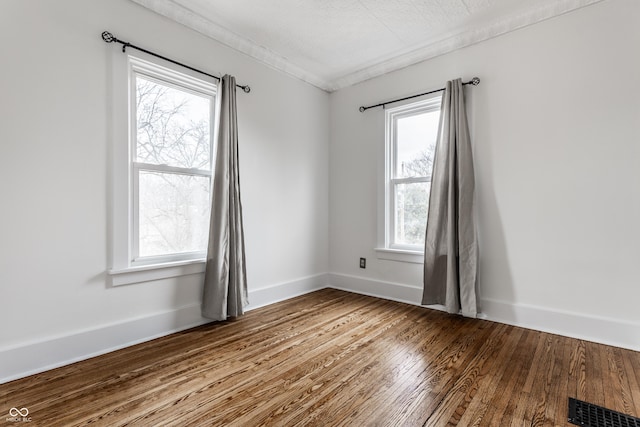 empty room featuring wood-type flooring, crown molding, visible vents, and baseboards