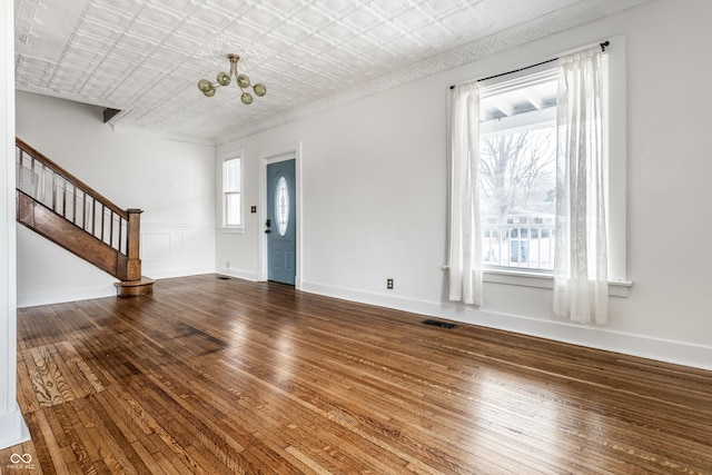 unfurnished living room with visible vents, stairway, hardwood / wood-style floors, an ornate ceiling, and an inviting chandelier