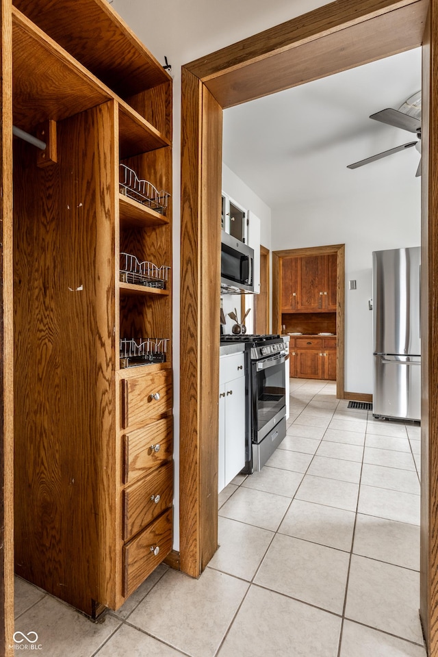 kitchen featuring light tile patterned floors, appliances with stainless steel finishes, a ceiling fan, and brown cabinets