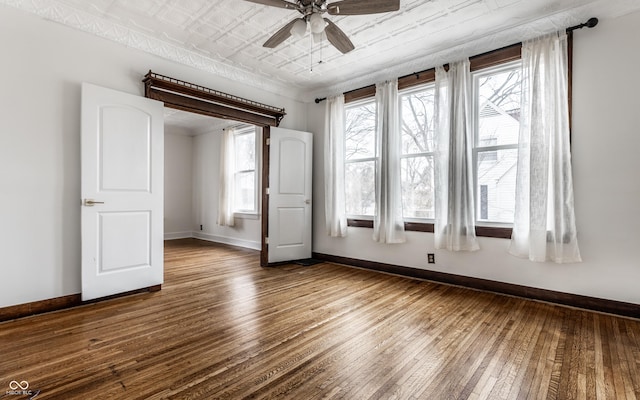 unfurnished room featuring a ceiling fan, an ornate ceiling, baseboards, and dark wood-type flooring