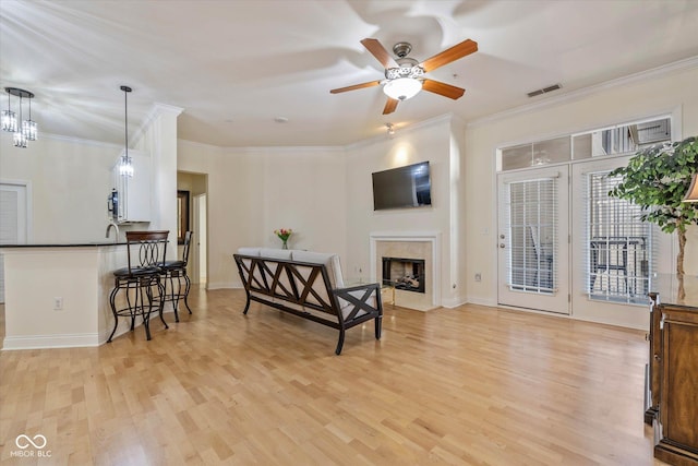 sitting room with light wood-style floors, a fireplace, visible vents, and ornamental molding