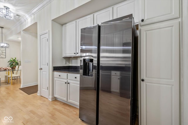 kitchen featuring light wood finished floors, stainless steel fridge, white cabinets, ornamental molding, and an inviting chandelier