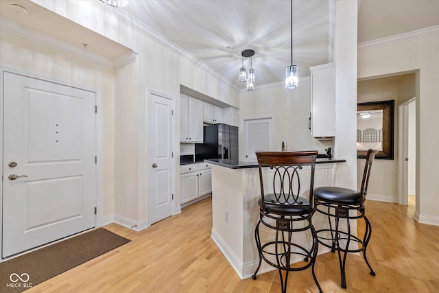 kitchen with white cabinets, dark countertops, a peninsula, a kitchen bar, and refrigerator with ice dispenser