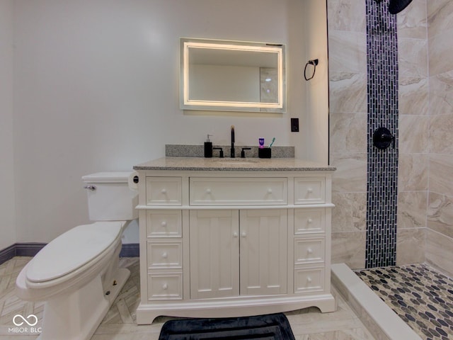 bathroom with baseboards, tiled shower, vanity, and toilet