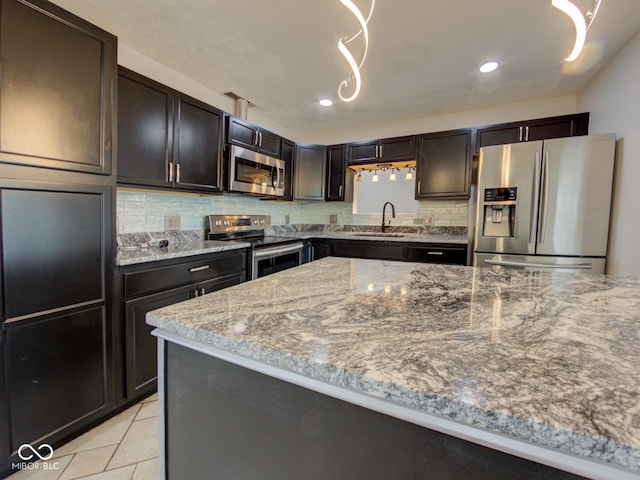 kitchen with light stone counters, light tile patterned flooring, a sink, appliances with stainless steel finishes, and decorative backsplash