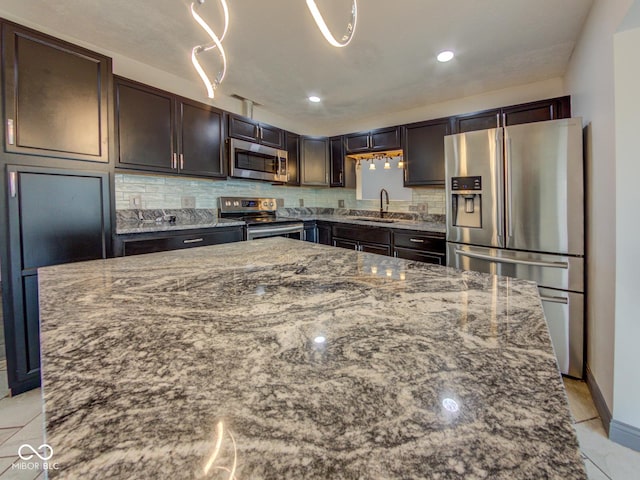 kitchen with appliances with stainless steel finishes, dark stone counters, a sink, and backsplash