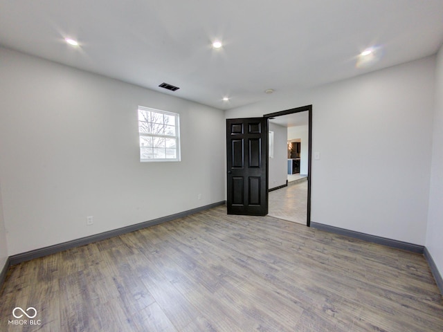 spare room featuring a barn door, recessed lighting, wood finished floors, visible vents, and baseboards