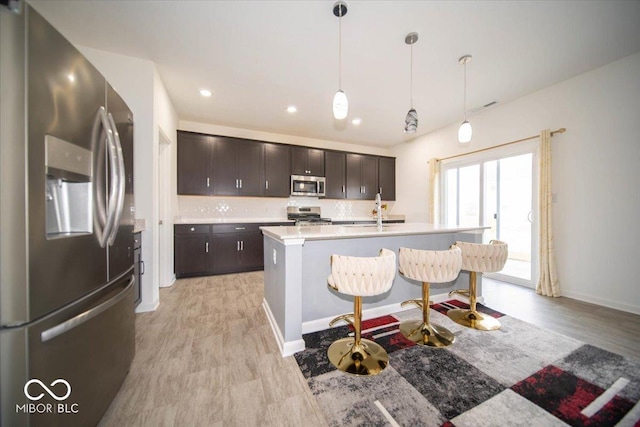 10202 Meadow Path Ln, Indianapolis, IN 46239 - kitchen with appliances with stainless steel finishes, light countertops, dark brown cabinetry, an island with sink, and hanging light fixtures