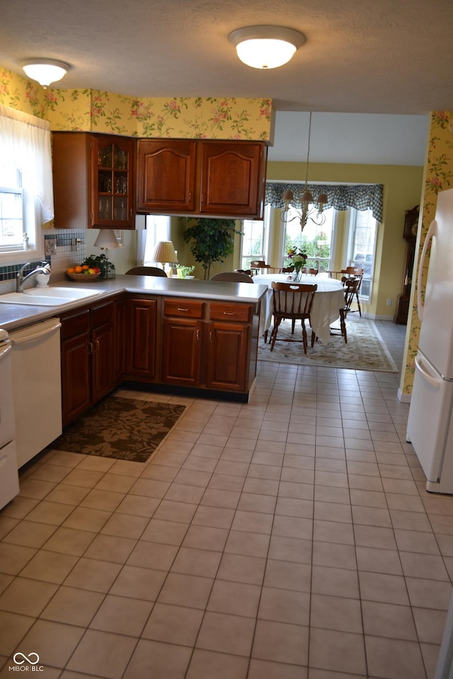 kitchen featuring white appliances, glass insert cabinets, a peninsula, light countertops, and a sink