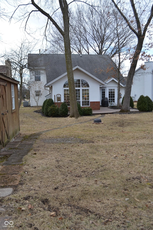 view of front of property with a shingled roof, a patio, an outbuilding, a storage unit, and brick siding