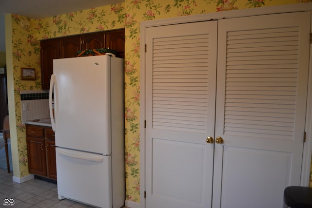 kitchen featuring light tile patterned floors, baseboards, light countertops, freestanding refrigerator, and wallpapered walls