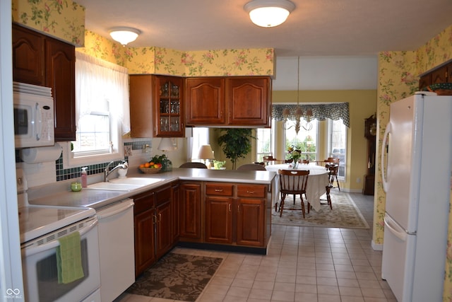 kitchen with a peninsula, white appliances, a sink, light countertops, and wallpapered walls