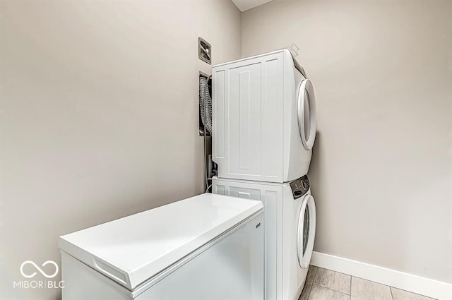 clothes washing area with light tile patterned floors, baseboards, stacked washer and clothes dryer, and laundry area